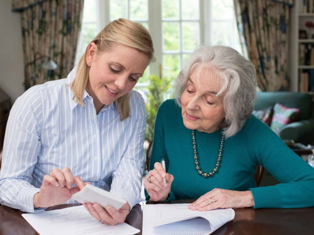 A caregiver and an elderly woman discussing financial documents at a table.