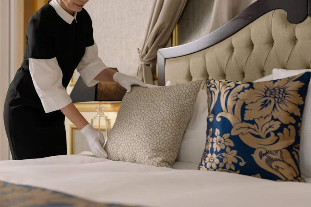 A hotel staff member arranging decorative pillows on a neatly made bed.