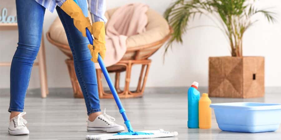Person mopping the floor with cleaning supplies in an NDIS-supported home environment