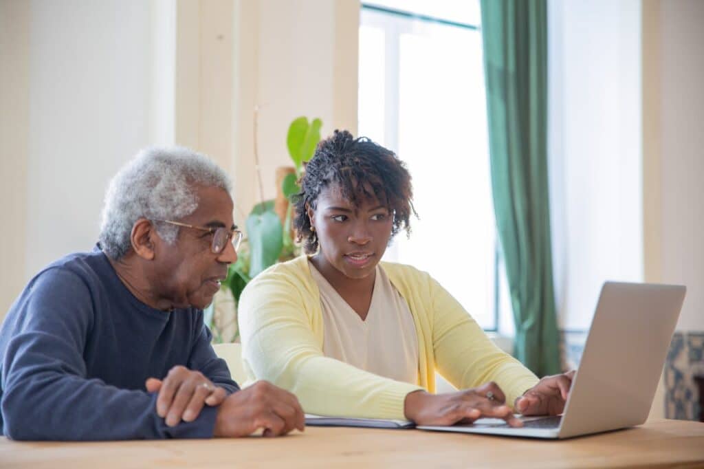 An elderly man and a young woman collaborating on a laptop.