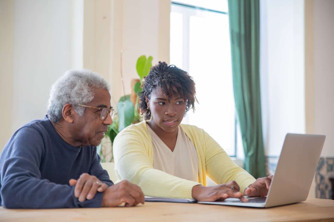 An elderly man and a young woman collaborating on a laptop.