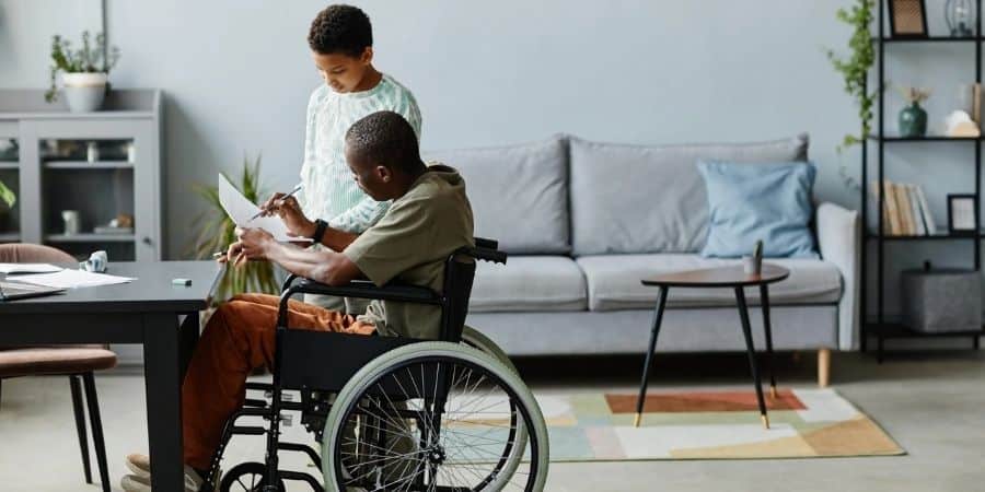 A father in a wheelchair assisting his son with learning activities at home.
