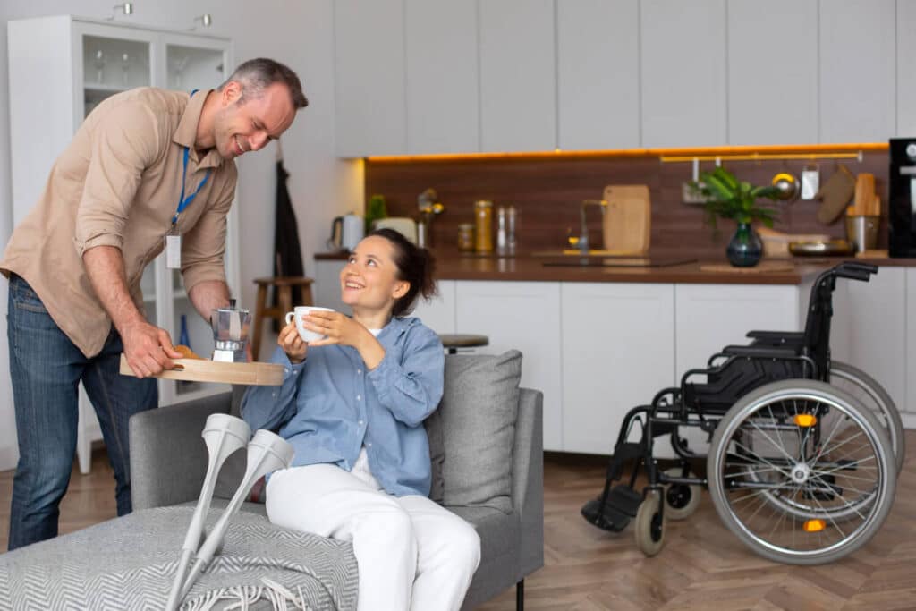 A caregiver serving coffee to a smiling woman in a cozy living room.