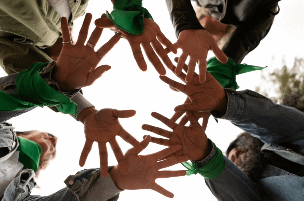 A circle of diverse hands with green bandanas, symbolizing unity and collaboration.