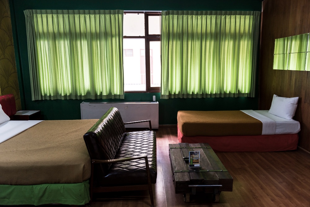 A cozy hotel room featuring green curtains, a double bed, and a single bed.