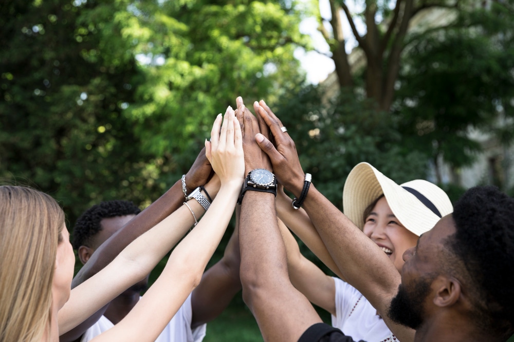 A diverse group of friends celebrating with high fives outdoors.