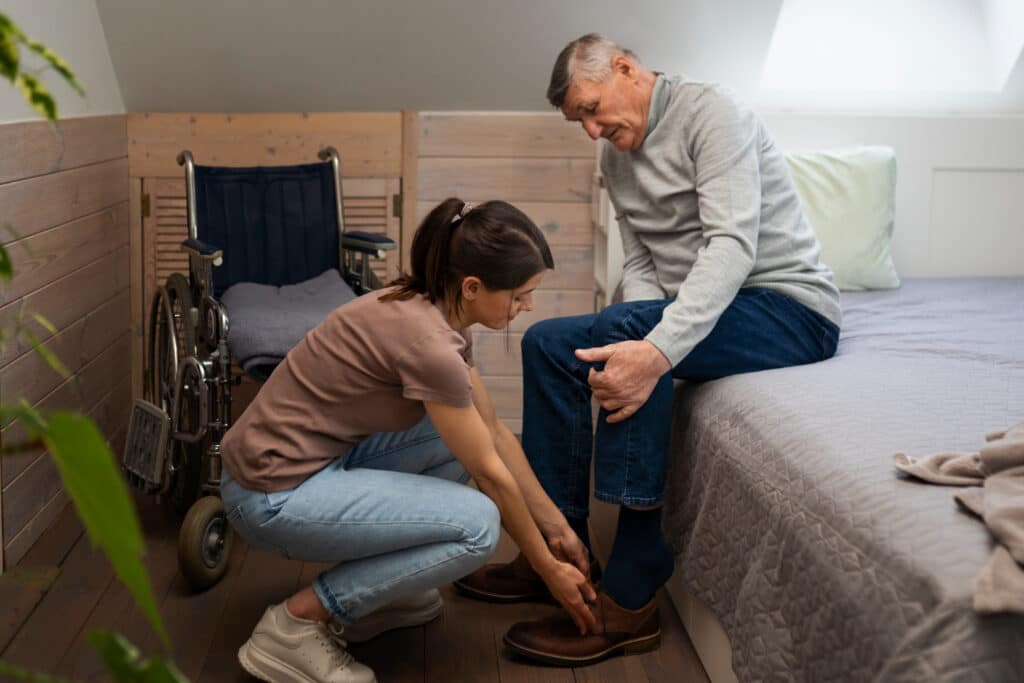 A caregiver helping an elderly man put on his shoes in a cozy room.