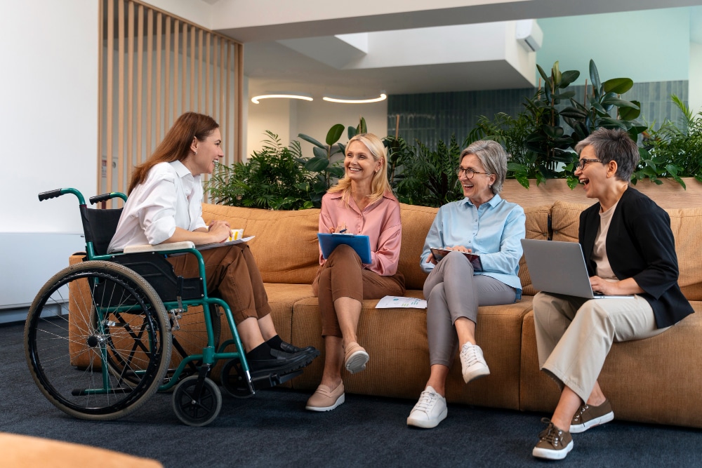 A group of four women, including one in a wheelchair, engaged in a lively discussion on a couch.
